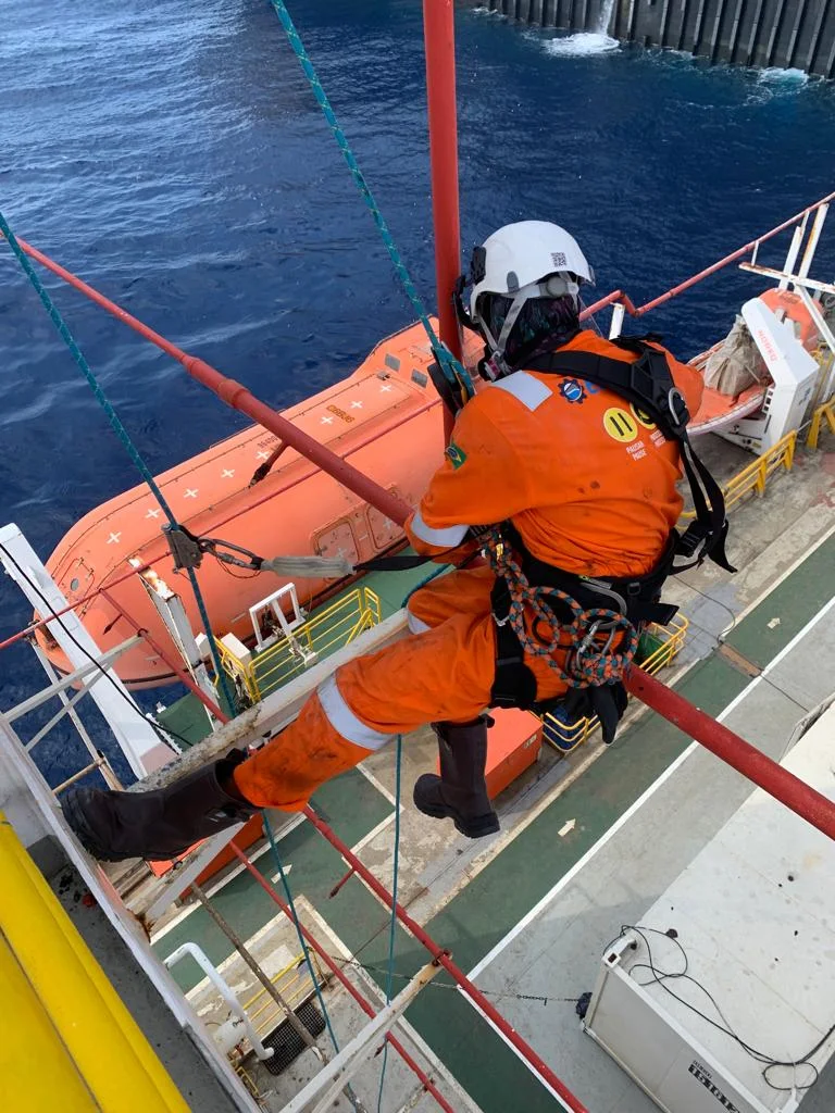 Técnico de acesso por cordas em descida controlada na lateral de uma unidade offshore